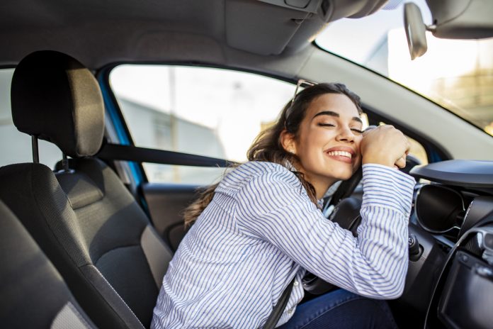 Young and cheerful woman enjoying new car hugging steering wheel sitting inside