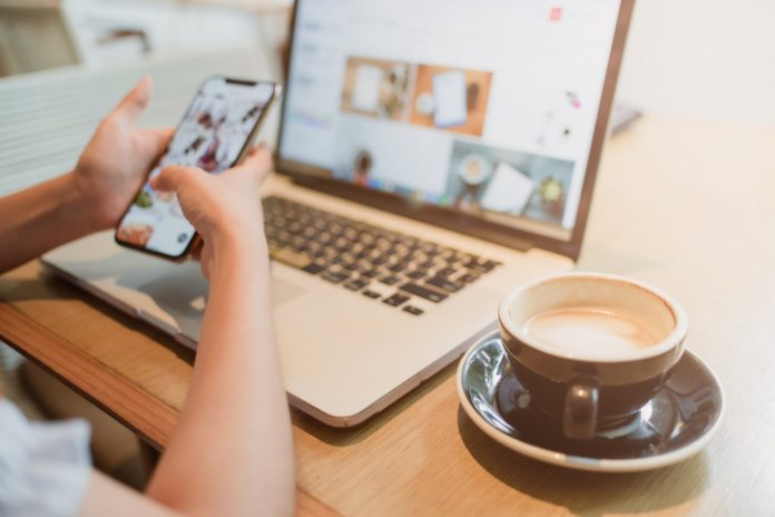 A woman sitting using a laptop and smartphone while eating coffee online security risks