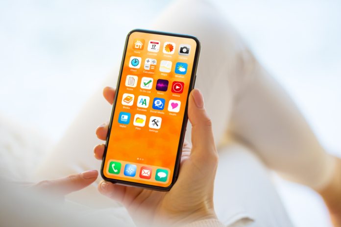 Woman using mobile phone with home screen opened showing different everyday app icons