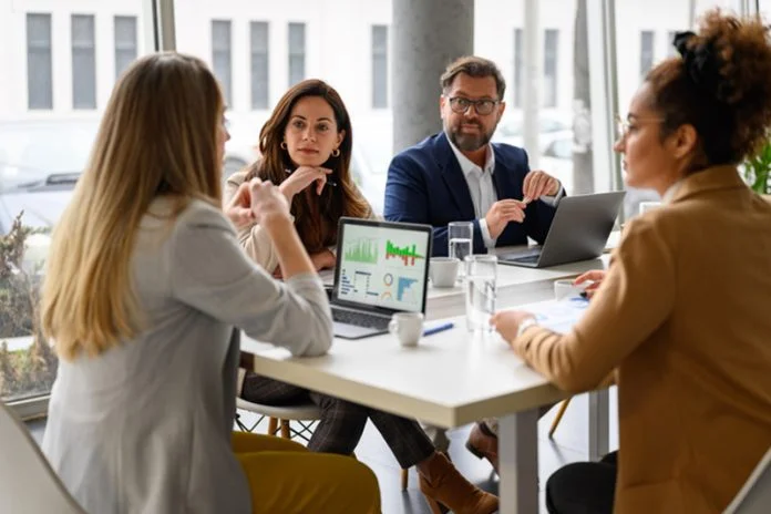 Businesswoman reviewing report on her laptop while discussing business growth with coworkers in meeting Expert Advisor Performance