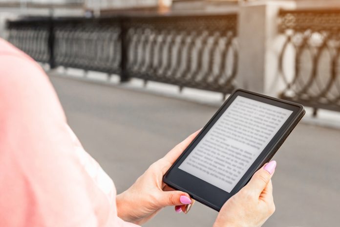 woman reading e-book sitting on bench in city park.