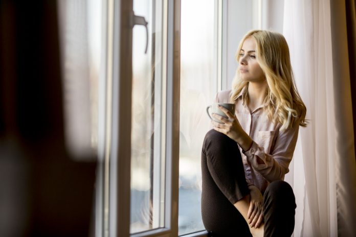 Blonde young woman drinking coffee by window