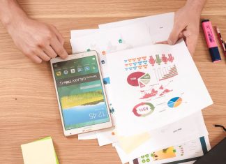 Person holding a white Samsung tablet and looking at a printout of charts