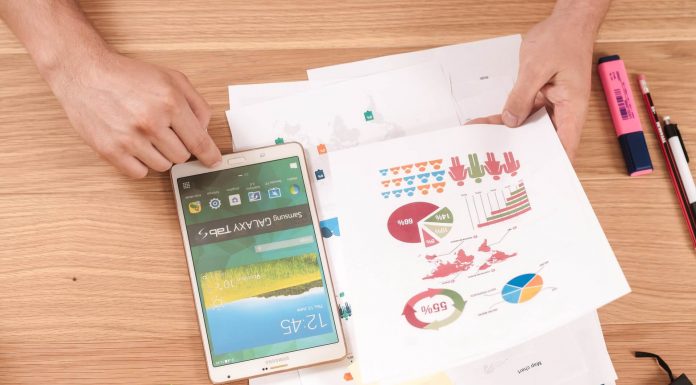 Person holding a white Samsung tablet and looking at a printout of charts