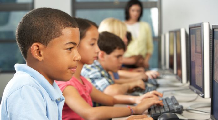 Elementary Students Working At Computers In Classroom Using Keyboard Concentrating