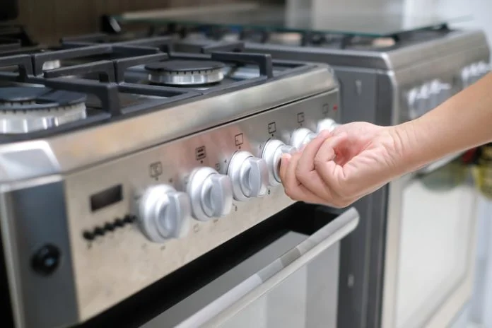 Male hand turning temperature knob of modern oven in kitchen showroom. Buying cooking appliance for domestic kitchen. Home improvement concept appliance repair San Jose