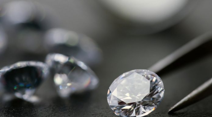 brilliant cut diamond held by tweezers on black background