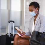 Business woman in airport with face mask checking phone