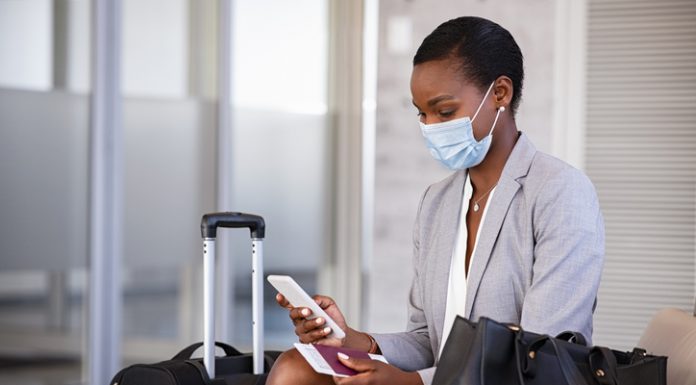 Business woman in airport with face mask checking phone