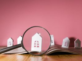 Magnifying glass in front of an open newspaper with paper houses. Concept of rent, search, purchase real estate.