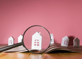 Magnifying glass in front of an open newspaper with paper houses. Concept of rent, search, purchase real estate.