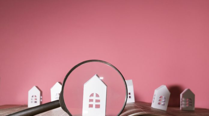 Magnifying glass in front of an open newspaper with paper houses. Concept of rent, search, purchase real estate.
