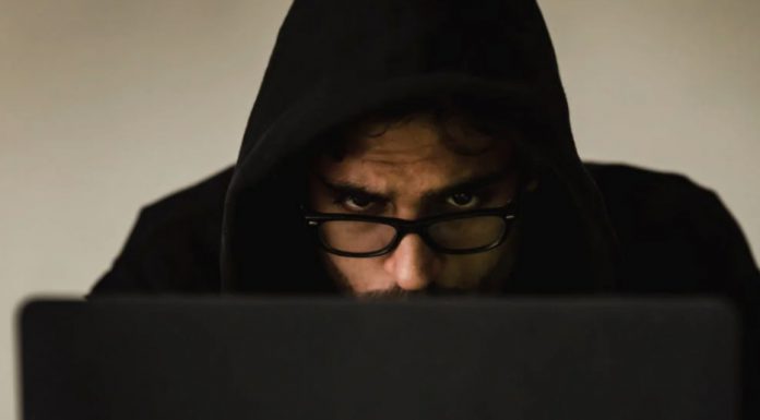 Should You Worry About China When Video Conferencing? Close up view of suspicious-looking man’s face wearing a hood, slumped over working on a laptop.