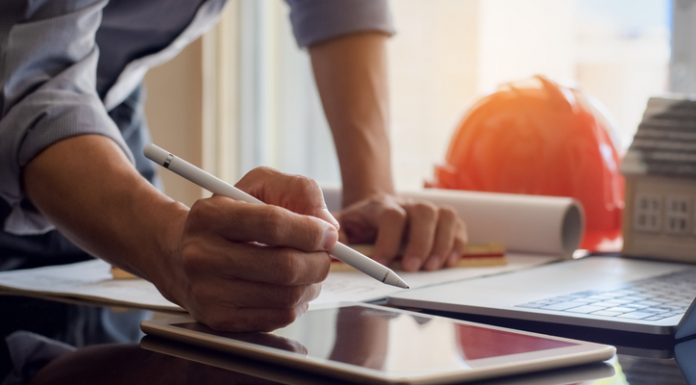Architect man or male engineer work on digital tablet with blue print and laptop computer on the desk at office.