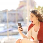 Amazed woman with smart phone content in the street