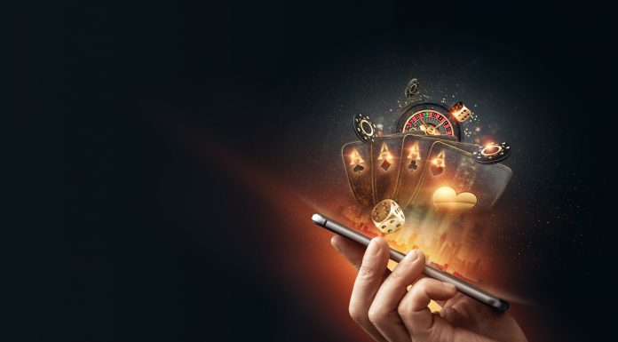 Creative background, online casino, in a man's hand a smartphone with playing cards, roulette and chips, black-gold background. Internet gambling concept. Copy space