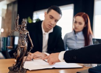 Pre-Settlement Funding: Is It an Answer to Someone’s Prayers? Statue of Themis holds scales of justice. In unfocused background, adult man signs documents.