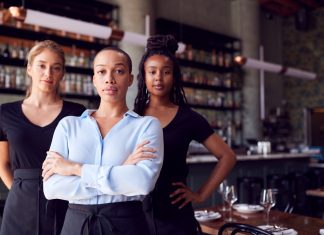 ‘Girlboss’ Went From Empowerment to Hypocrisy. How Should We Talk About Young Women’s Ambition Now? Portrait Of Female Owner Of Restaurant Bar With Team Of Waiting Staff Standing By Counter