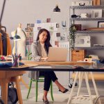 How to Improve Your Small Business: Budget-Friendly Tips and Advice Female Fashion Designer In Studio Working On Sketches Or Documents At Desk With Laptop