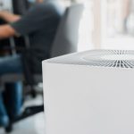 Blast Auxiliary Air Cleaner Review: Is the Blast Air Cleaner Actually Good? Close up Air purifier in the room is very safe and clean to breathe with filter dust PM 2.5 and a man use computer desktop working in home in clean air