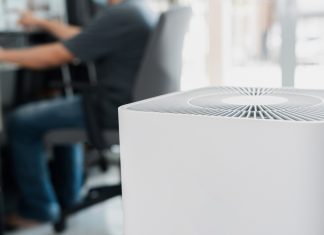Blast Auxiliary Air Cleaner Review: Is the Blast Air Cleaner Actually Good? Close up Air purifier in the room is very safe and clean to breathe with filter dust PM 2.5 and a man use computer desktop working in home in clean air
