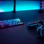 Gaming accessories on dark table. Keyboard with color backlit and stereo headphones.