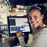 Smiling African waitress using a restaurant point of sale terminal