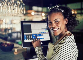 Smiling African waitress using a restaurant point of sale terminal
