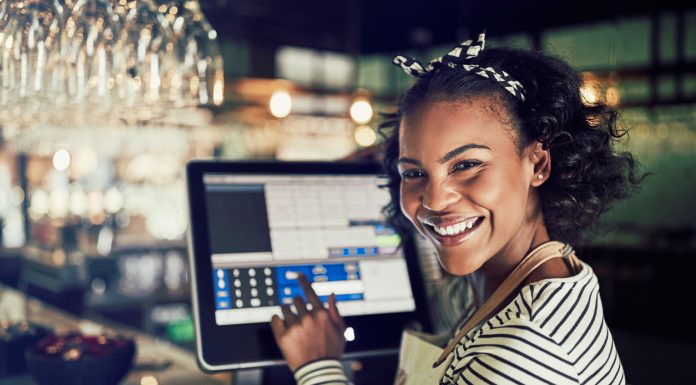 Smiling African waitress using a restaurant point of sale terminal