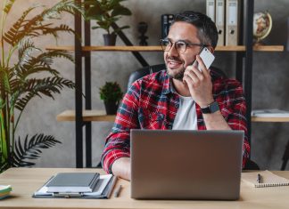 Portrait of smiling grey hair man with beard sitting front table with laptop, talking on phone