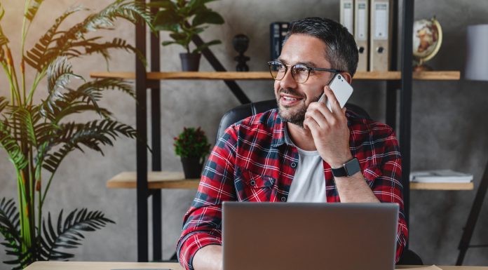 How are Manufacturers Embracing Work from Home Culture Portrait of smiling grey hair man with beard sitting front table with laptop, talking on phone