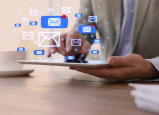 Businessman sending emails at wooden table in office, closeup