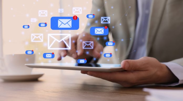 Businessman sending emails at wooden table in office, closeup