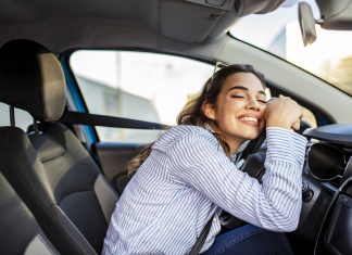 Young and cheerful woman enjoying new car hugging steering wheel sitting inside