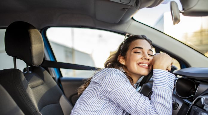 Young and cheerful woman enjoying new car hugging steering wheel sitting inside