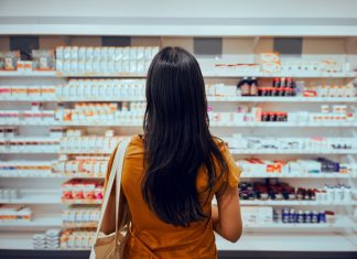 Genomics and Rare Diseases: The Advent of Personalised Medicine? Rear view of young woman with bag standing against shelf in pharmacy searching for medicine