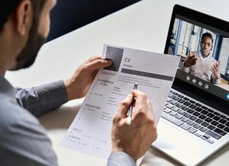 5 Things Recruiters Look At Before Hiring Male indian hr, recruiter or employer holding cv having online virtual job interview meeting with african candidate on video call. Distance remote recruitment conference chat. Over shoulder view.