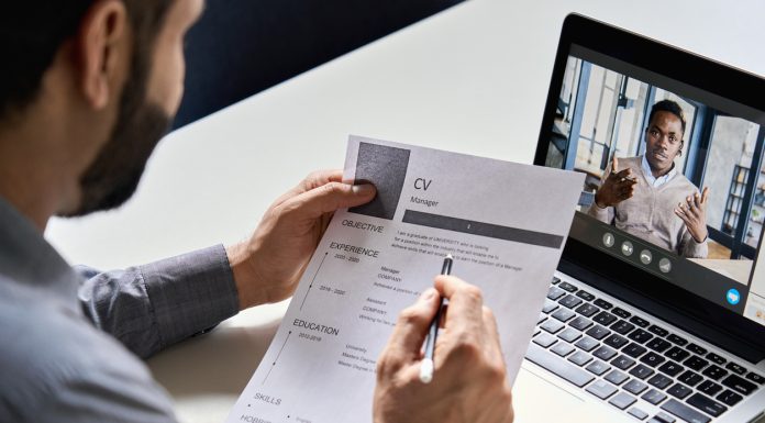 Male indian hr, recruiter or employer holding cv having online virtual job interview meeting with african candidate on video call. Distance remote recruitment conference chat. Over shoulder view.