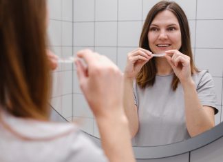Close up of a woman in front of a mirror in the bathroom putting on invisible plastic teeth aligners or braces. Beautiful and healthy smile. Teeth whitening.