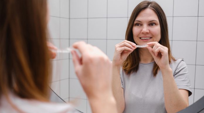 Close up of a woman in front of a mirror in the bathroom putting on invisible plastic teeth aligners or braces. Beautiful and healthy smile. Teeth whitening.