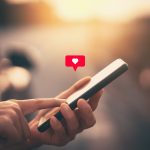 Close up woman hand hold using smart phone with heart icon at outdoor park street background. Copy space of technology business and travel holiday concept.