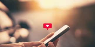 Close up woman hand hold using smart phone with heart icon at outdoor park street background. Copy space of technology business and travel holiday concept.