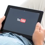 man holding iPad with app YouTube on the screen