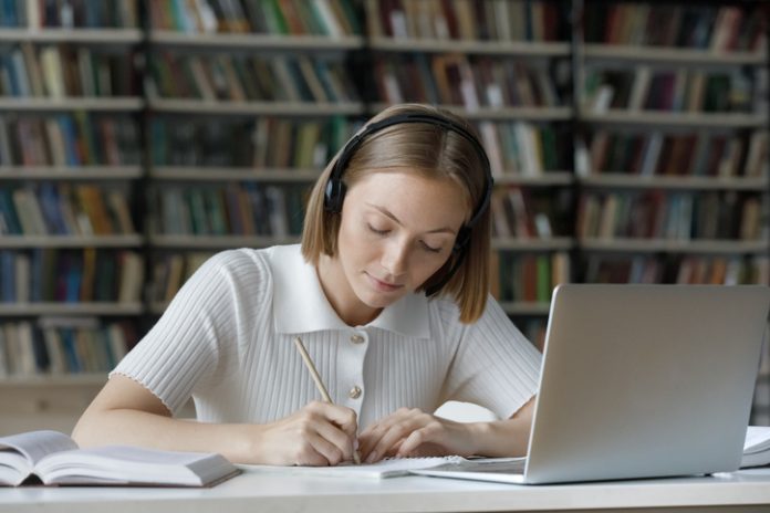 Serious student girl listening to audio tutorials from wireless headphones,