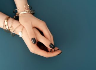 Female hands with trendy dark nail design with gold bracelets on aqua background. Luxury concept. Festive backdrop for your design.