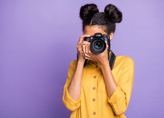 Photo of amazing dark skin lady holding photo digicam in hands photographing foreign sightseeing abroad wear yellow shirt trousers isolated purple color background