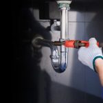 Plumber fixing white sink pipe with adjustable wrench.