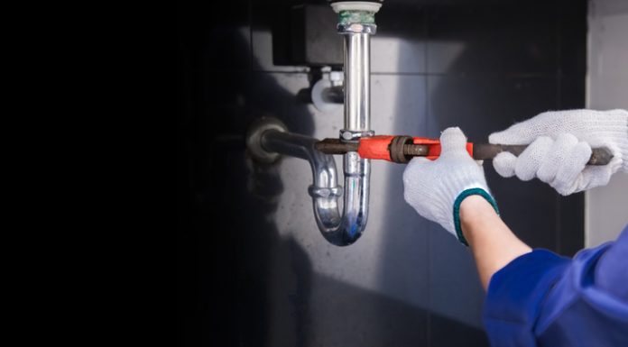 Plumber fixing white sink pipe with adjustable wrench.