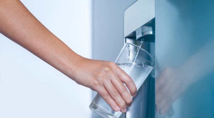 Water dispenser from dispenser of home fridge, Woman is filling a glass with water from the refrigerator.