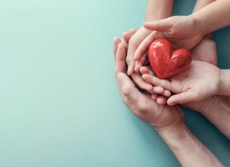 How Can Your Emotional Health Impact Your Skin? adult and child hands holding red heart on aqua background, heart health, donation, CSR concept, world heart day, world health day, family day